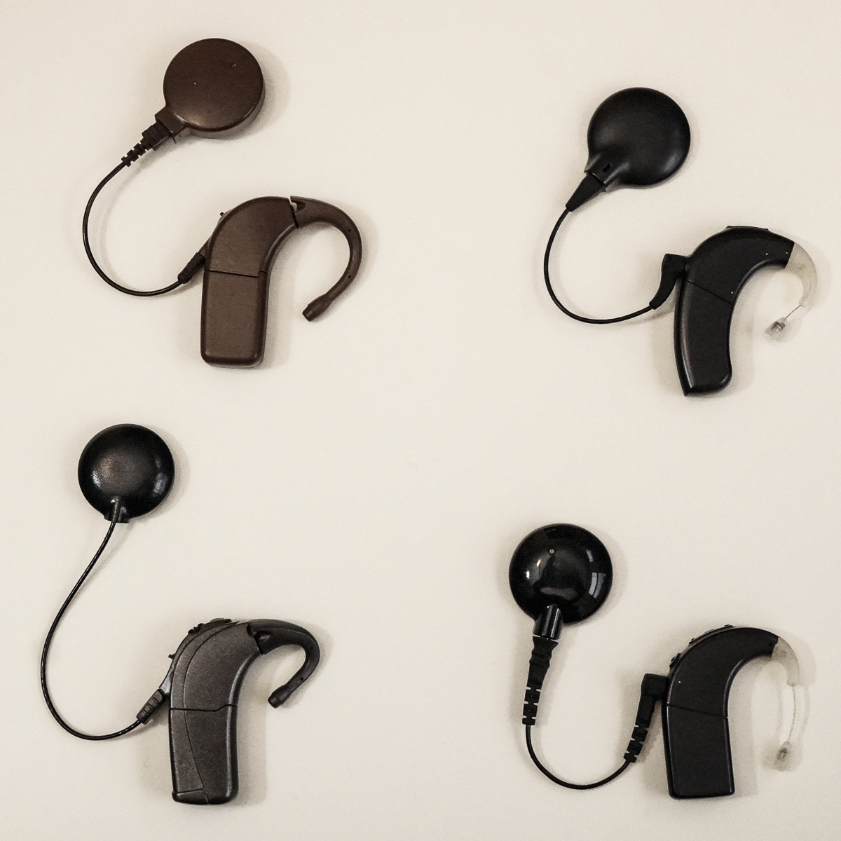 Four behind-the-ear cochlear implant sound processors from successive product generations, shown side by side, each smaller than the last.