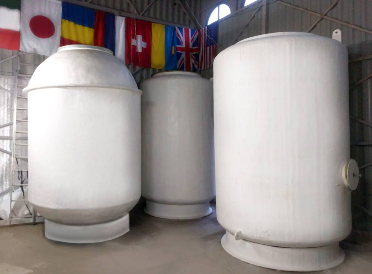 Three large white fibreglass dewars, person-height cylinders with domed lids, standing on a concrete floor in a metal-walled warehouse hung with national flags.